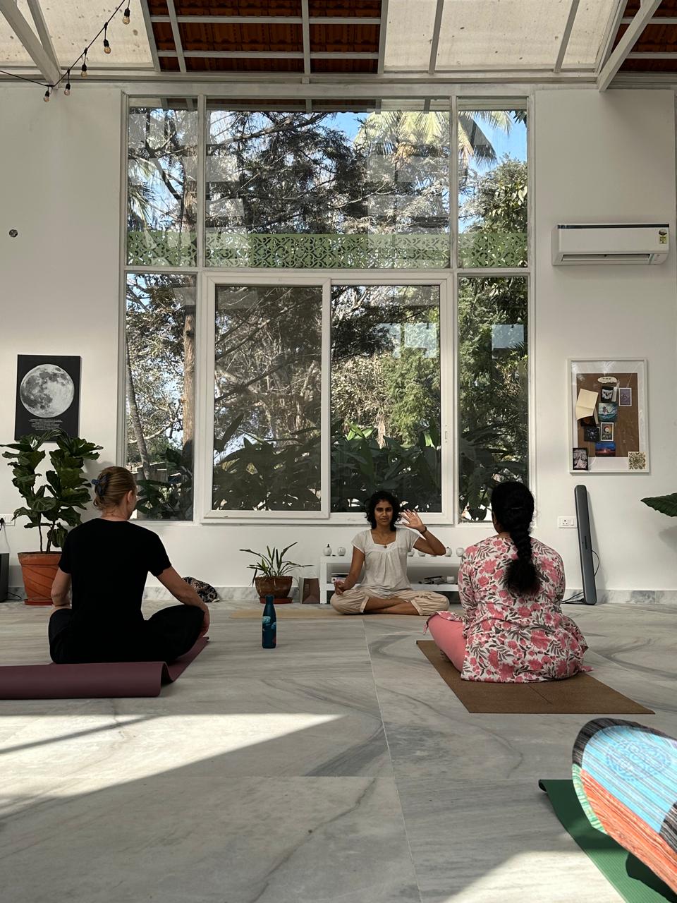 Likhitha guiding two seated students in the studio beneath a moon art print — in-session teaching