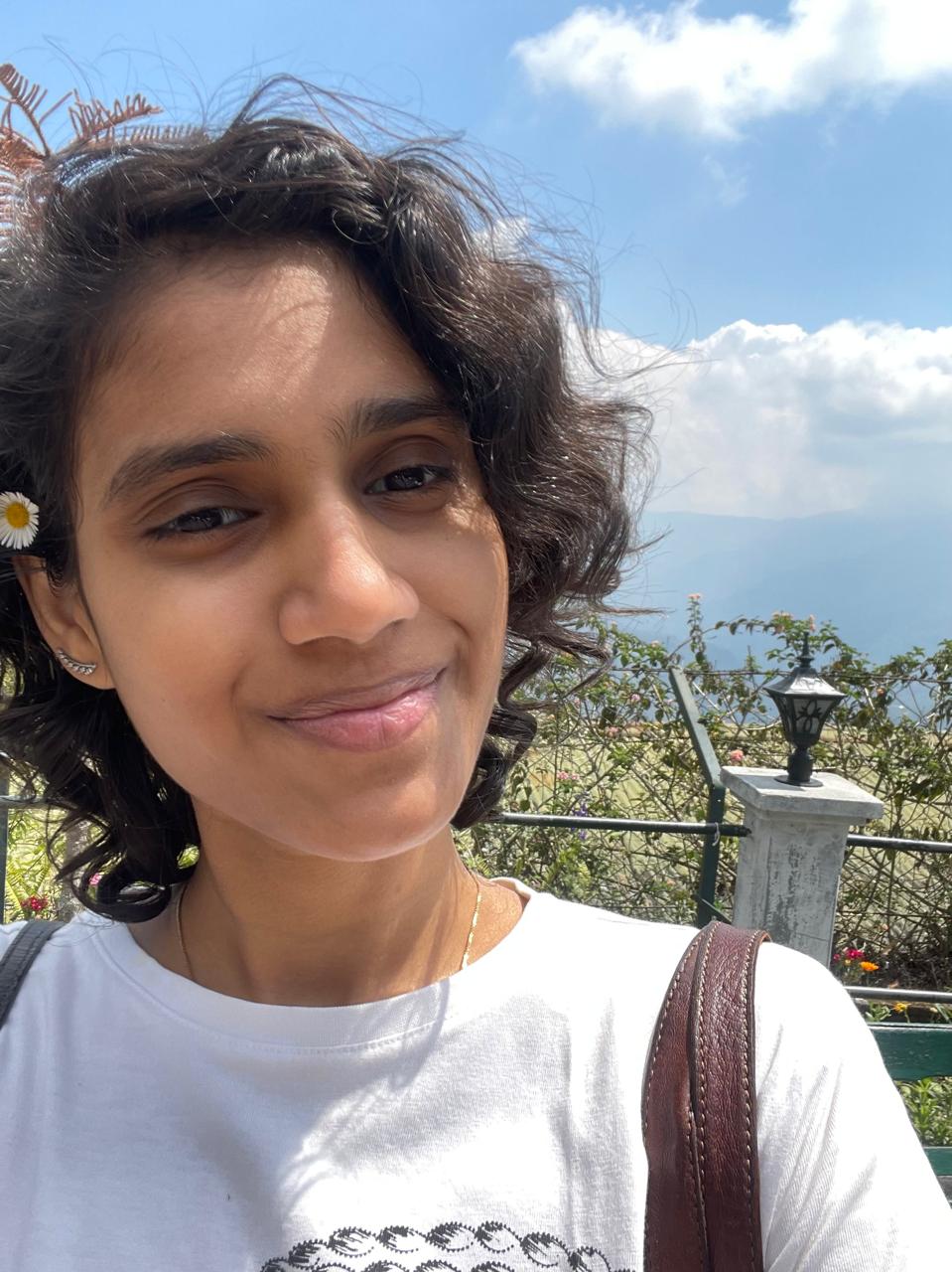 Likhitha Sree at a hillstation, smiling in a white daisy tee