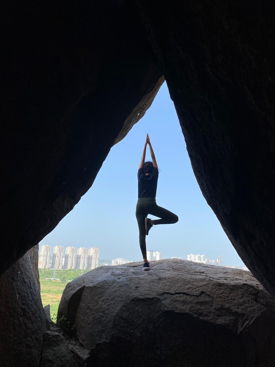 Likhitha in tree pose framed by rocks with a cityscape behind her
