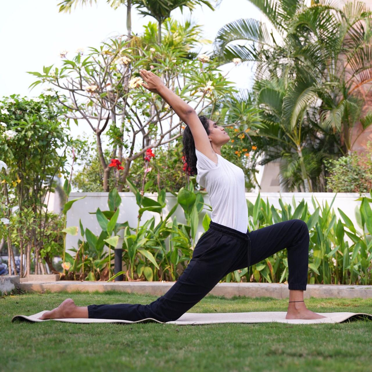 Likhitha Sree in a crescent lunge in a tropical garden — outdoor practice