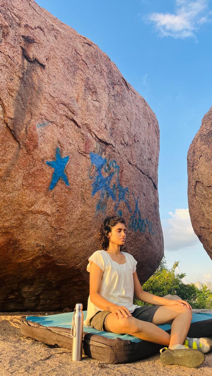 Likhitha Sree seated in meditation at golden hour, red boulders behind her